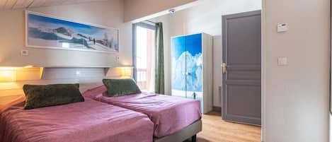 A bedroom with two beds, a large window with a mountain view, and a door leading to another room.