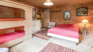 Une pièce de cabane en bois comprenant des lits superposés, un lit simple, une chaise, un bureau et une lampe.