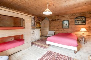 A wooden cabin room with bunk beds, a single bed, a chair, a desk, and a lamp.