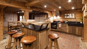 Une cuisine rustique avec des poutres en bois, un îlot central doté de tabourets, une cuisinière et un évier.