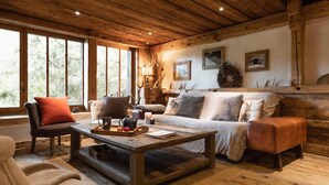 L’intérieur d’un chalet rustique, avec un plafond en bois, de grandes fenêtres, un canapé, un fauteuil et une table basse sur laquelle se trouve un plateau de pommes.