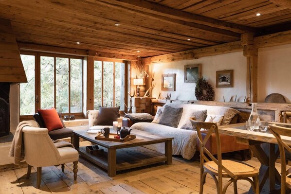 A cozy cabin interior with a fireplace, wooden furniture, and large windows.