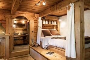 A rustic wooden room with a bed, a small sink, and a shelf with jars.