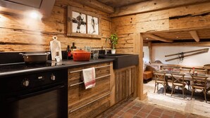 Une cuisine rustique aux murs en bois, dotée d’un plan de travail noir et d’un coin repas avec des chaises et une table en bois.