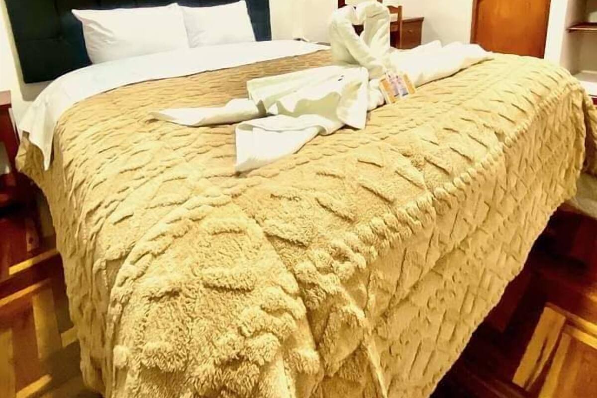 Une chambre d’hôtel avec un grand lit, une tête de lit, un plancher en bois, un tableau au mur, un miroir et une porte en bois.