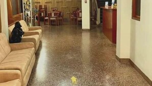 Een hotel lobby met een receptiebalie, een zithoek met een bank en een trap naar een andere verdieping.