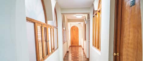 A hallway with wooden flooring, arched windows, and a wooden door.