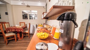 Een ontbijt opstelling met een koffiezetapparaat, een fruitschaal en sap op een houten tafel.