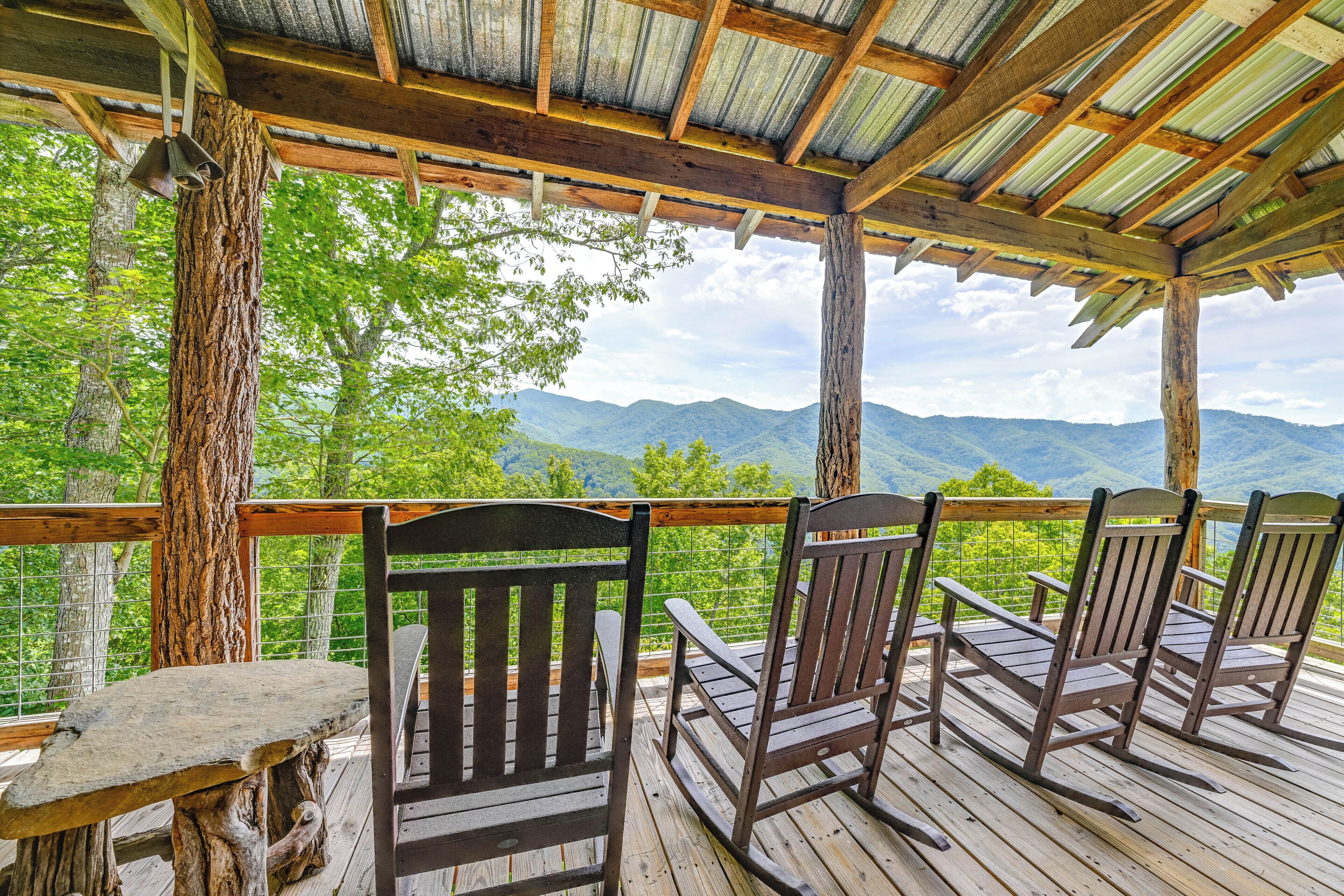 Una terraza de madera con mecedoras y una mesa, con vistas a un paisaje montañoso.