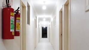 A long, narrow hallway with white tiled floors and walls, equipped with fire extinguishers on the left wall. - Pousada Garoupa (Cabo Frio)