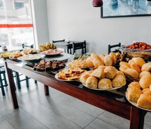 Un tavolo con buffet assortito, con pane, dolci e un piatto con salsa rossa.