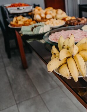 A buffet table with various food items including bananas, salads, and other dishes. - Pousada Garoupa (Cabo Frio)