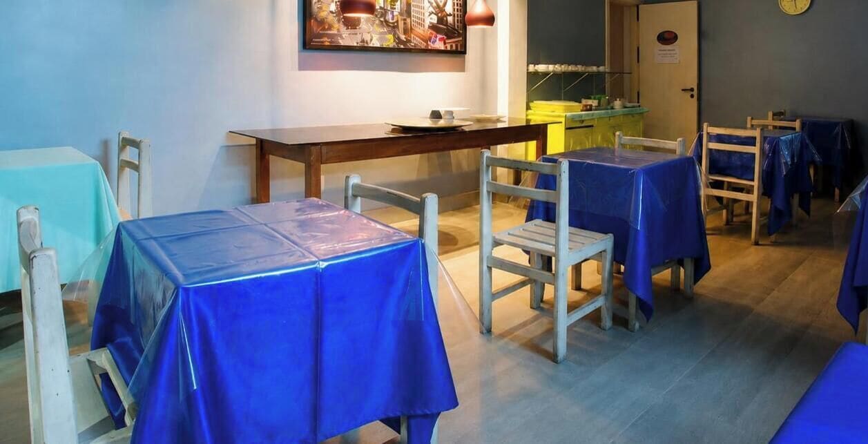 Un comedor con mesas cubiertas con manteles azules, sillas de madera y un cuadro en la pared.