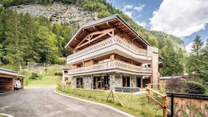 Un chalet en bois à plusieurs étages, doté d’un balcon, situé dans une région montagneuse sous un ciel dégagé.