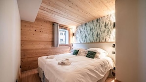 Une chambre avec un plafond en bois, un lit avec une literie blanche et une fresque murale sur le thème de la forêt.