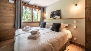 Una camera da letto con due letti, pareti in legno, una finestra con tende e un quadro appeso al muro, più una lampada da comodino.