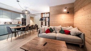 Un soggiorno moderno con una parete in legno, un divano con cuscini, un'area pranzo con sedie e una cucina sullo sfondo.