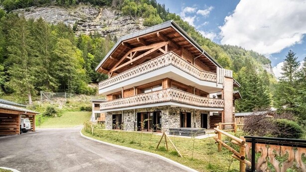 Un chalet in legno a più piani con un balcone, immerso in un paesaggio montano sotto un cielo sereno.