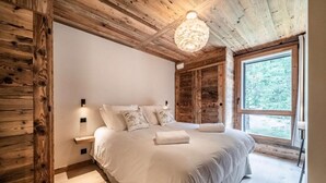 A bedroom with a wooden ceiling, a large bed with white linens, a nightstand, and a window with a view of trees. - 1st floor, balcony, parking, tv, ski locker, 93m², Morzine (Morzine)