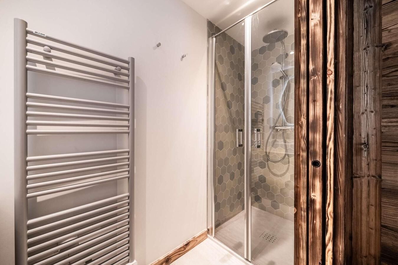 A modern bathroom with a glass shower enclosure, a white radiator, and wooden paneling.