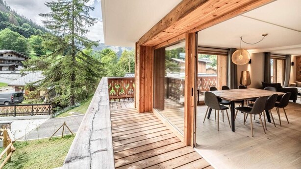 A modern interior with a wooden deck, a dining area with chairs, and a view of a mountainous landscape. - 1st floor, balcony, parking, tv, ski locker, 93m², Morzine (Morzine)