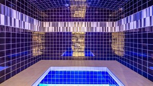 En modern inomhuspool med ett geometriskt kakelmönster och en central vattenfontän.