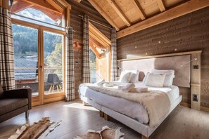 A cozy bedroom with a large bed, a wooden headboard, and a view of the outdoors through a sliding glass door. - 250m from ski lifts, 2nd floor, fitness, hammam, balcony, tv, ski locker, 137m², Morzine (Morzine)