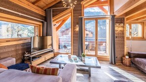 En mysig stuga med träpanel i taket, stora fönster, en tv och en soffa.