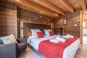 A cozy wooden room with a large bed, a chair, and a wooden wall.