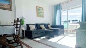 A living room with a sofa, a dining table, and a view of the outdoors. - Apartment Aguamarina 4B (Estepona)