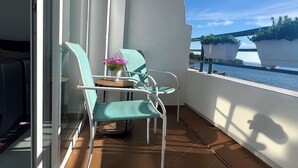 A balcony with two turquoise chairs, a small round table, and a potted plant with pink flowers. - Apartment Aguamarina 4B (Estepona)