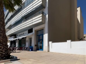 A modern building with a flat facade, a blue door, and a sign for 'Capriccio'. - Apartment Aguamarina 5C (Estepona)