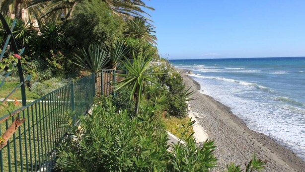A coastal walkway with a metal fence, lush greenery, and a view of the ocean. - Adosado junto al Mar (Estepona)