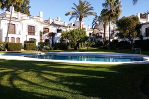 Une piscine entourée de pelouses bien entretenues et de palmiers, avec un bâtiment à l’arrière-plan dont l’architecture est de style traditionnel.
