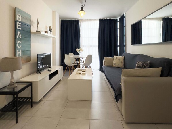 A modern living room with a sofa, coffee table, TV, and a desk with a lamp.