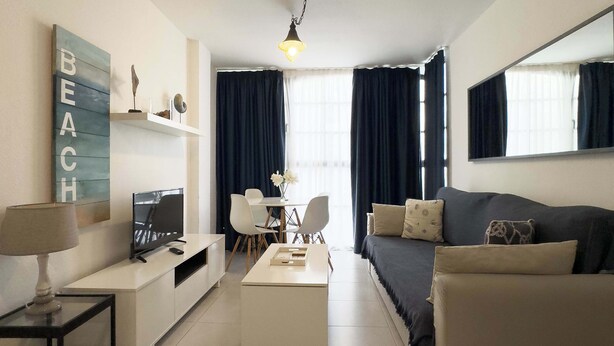Ein modernes Wohnzimmer mit Sofa, Couchtisch, Fernseher und Schreibtisch mit Lampe.
