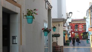 Eine schmale Straße mit hängenden Blumentöpfen und einem roten Gebäude im Hintergrund.
