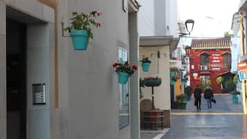 A narrow street with hanging flower pots and a red building in the background.