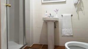 A bathroom with a glass shower door, a pedestal sink, a toilet, and a mirror above the sink.