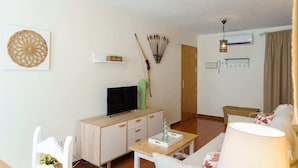 A living room with a TV, a wooden cabinet, a cactus, and a dining table.
