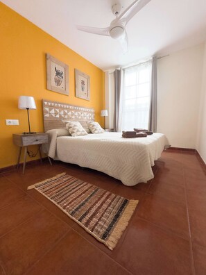 A bedroom with a bed, a standing lamp, a ceiling fan, and two framed pictures on the wall. - Cristamar Center and Beach Apartment 2B (Estepona)