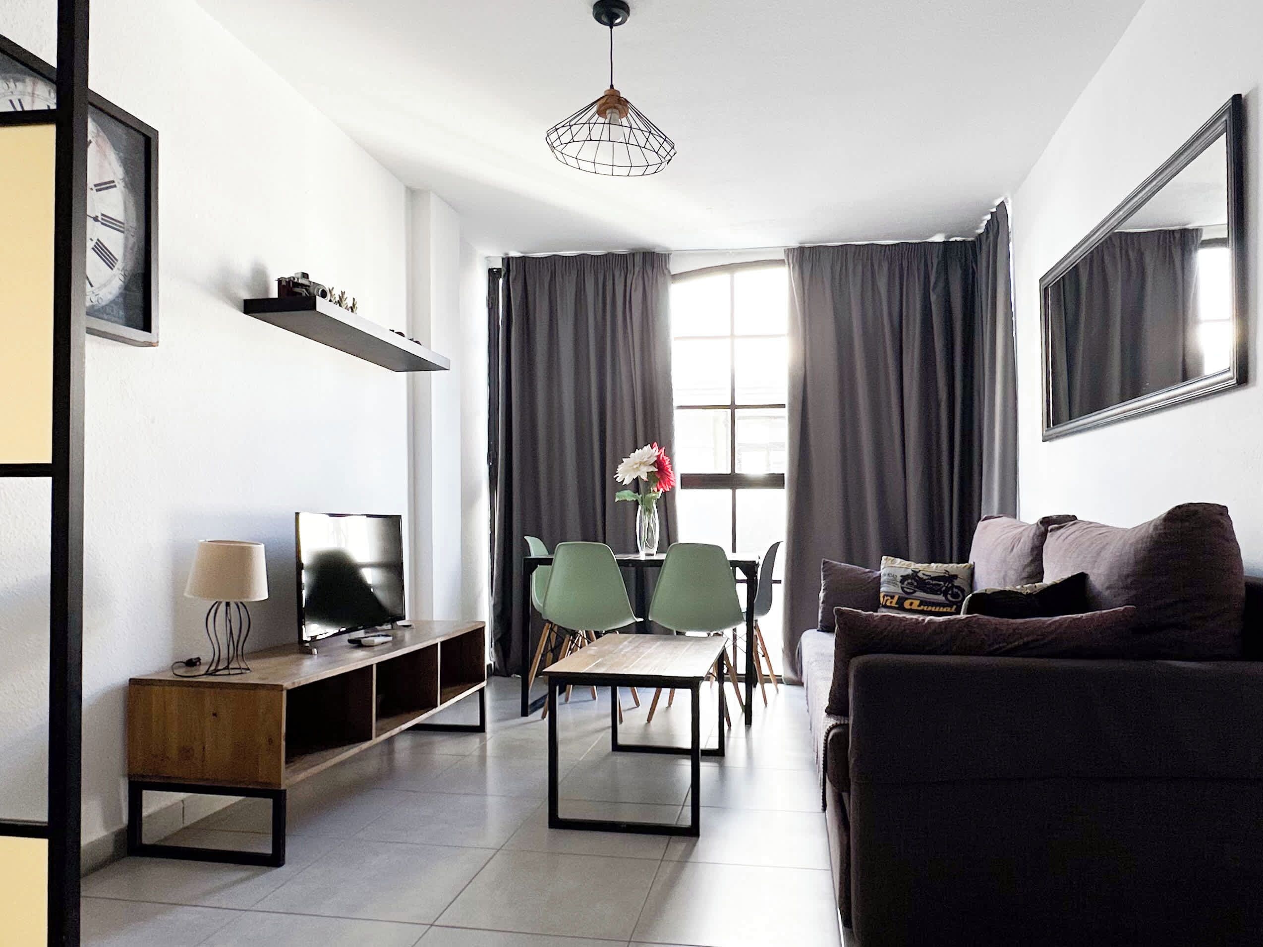 A modern living room with a sofa, TV, and a dining area with chairs and a table.