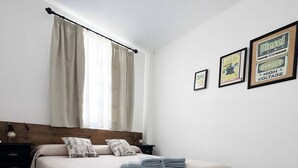 A bedroom with a bed, pillows, a nightstand, a window with curtains, and a rug.