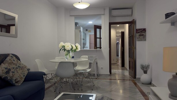 A modern living room with a blue sofa, a dining table with chairs, a coffee table with a decorative plate, and a vase with flowers. - Spacious Apartment, Seneca 1A next to the Center. (Málaga)