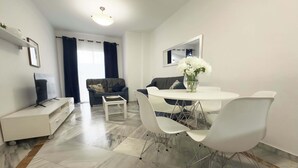 A modern living room with a sofa, a dining table with chairs, a TV, and a vase with flowers. - Spacious Apartment, Seneca 1A next to the Center. (Málaga)