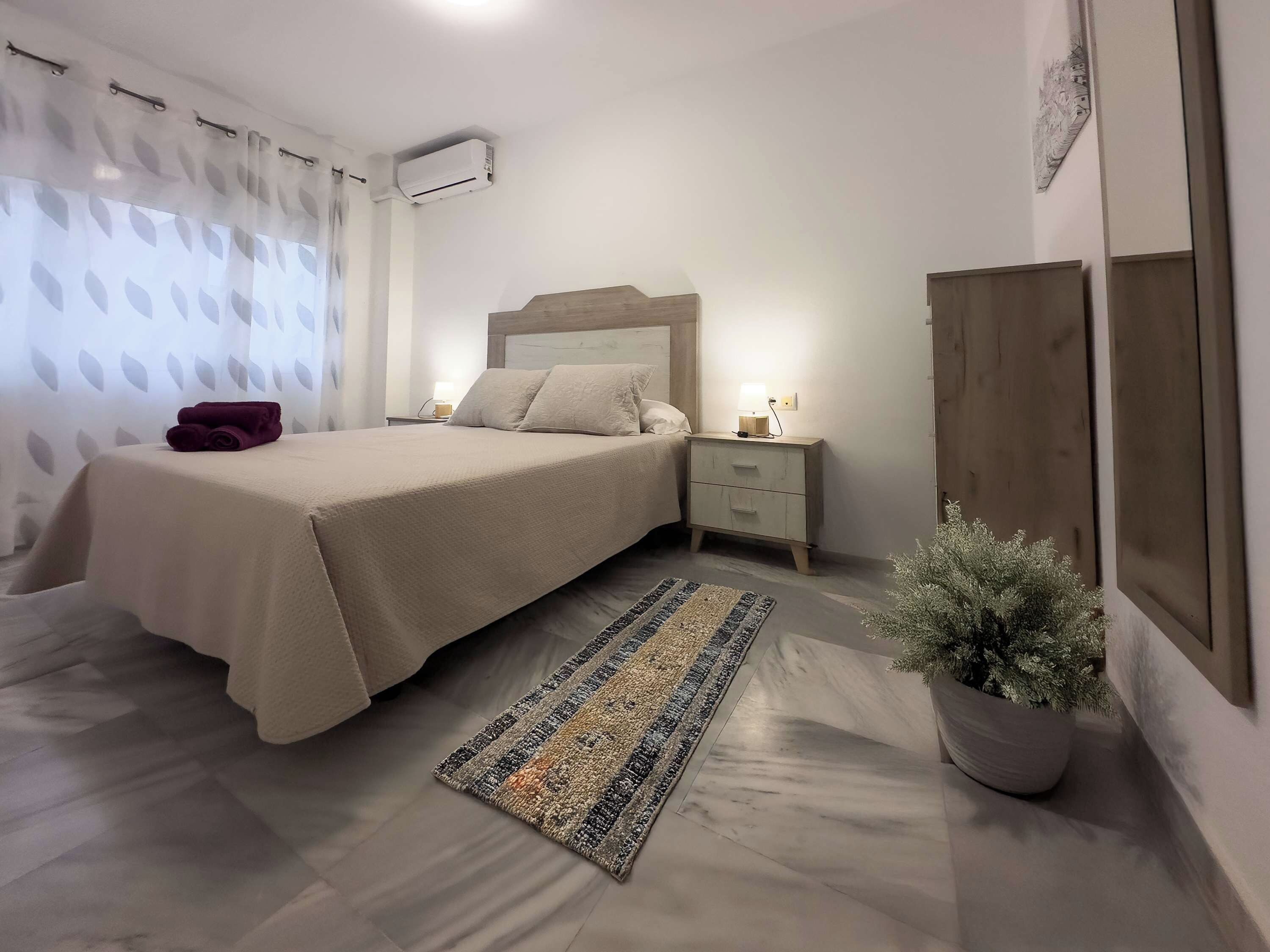 A neatly arranged bedroom with a bed, bedside table, nightstand, and a potted plant.