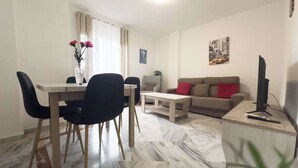 Uma sala de estar moderna com área de refeições, apresentando um sofá, mesa de centro e uma TV em um suporte.