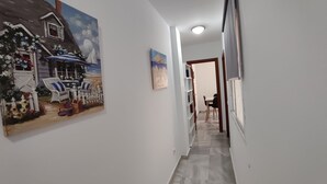 Um corredor com um quadro de uma cena de praia, uma pequena mesa com cadeiras e uma porta que dá para um quarto.