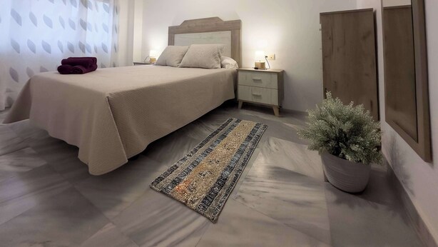 Quarto bem arrumado com cama, mesa de cabeceira, criadeira e um vaso de planta.