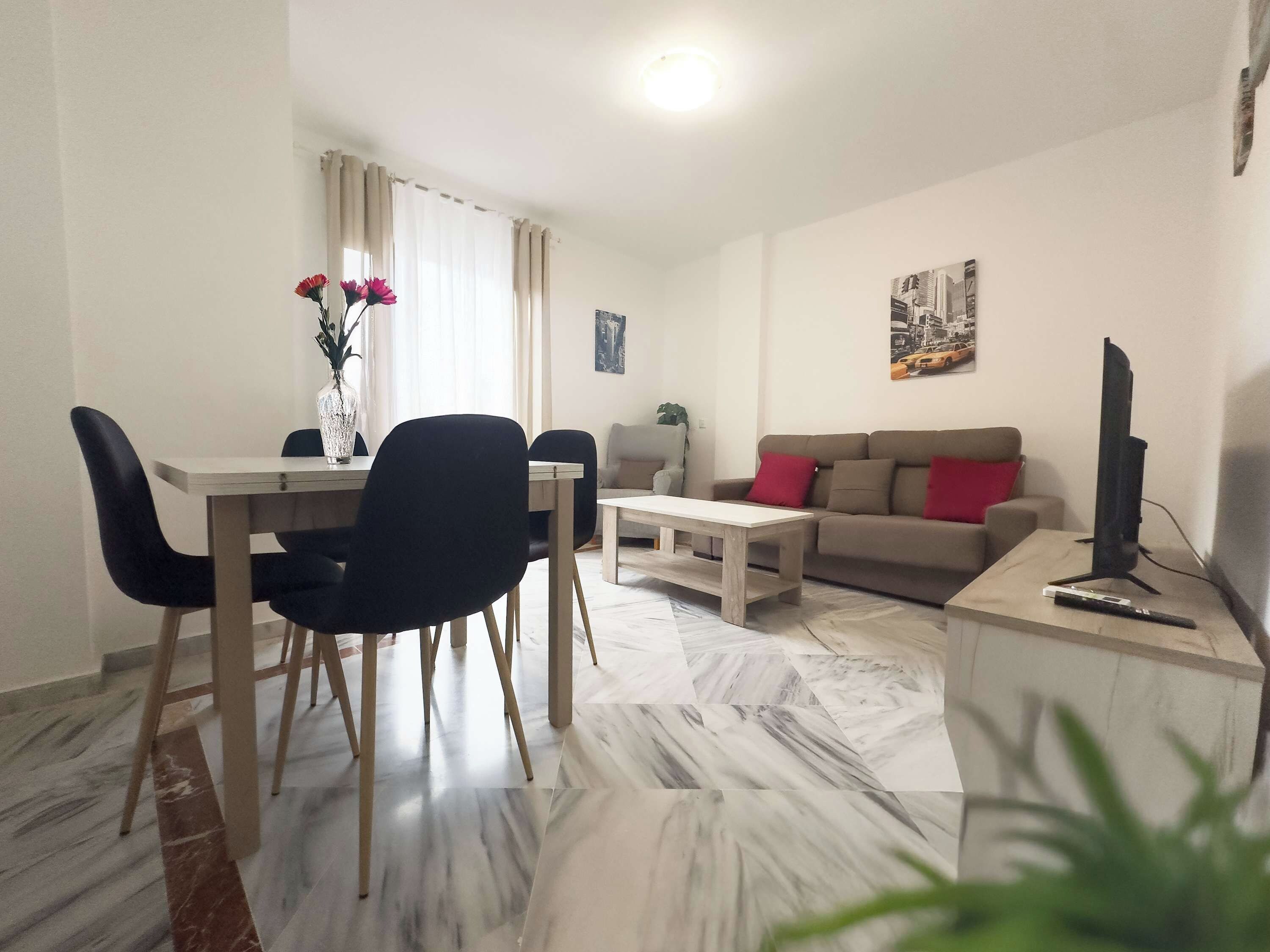 A modern living room with a dining area, featuring a sofa, coffee table, and a TV on a stand.